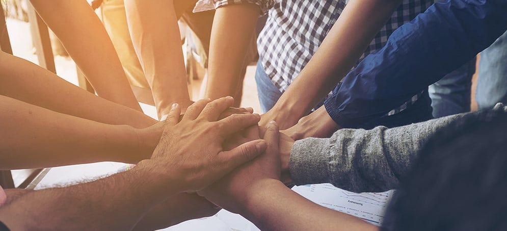 Teamhände die gemeinsam die Hände in die Mitte legen und sich festhalten