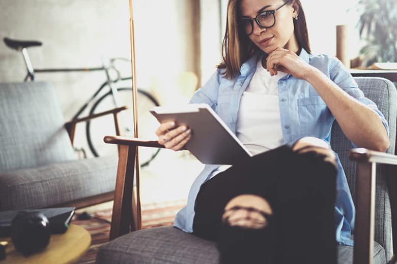 Eine Frau sitzt in einem Sessel und schaut auf ein Tablet. Der Inhalt wurde automatisiert erstellt.