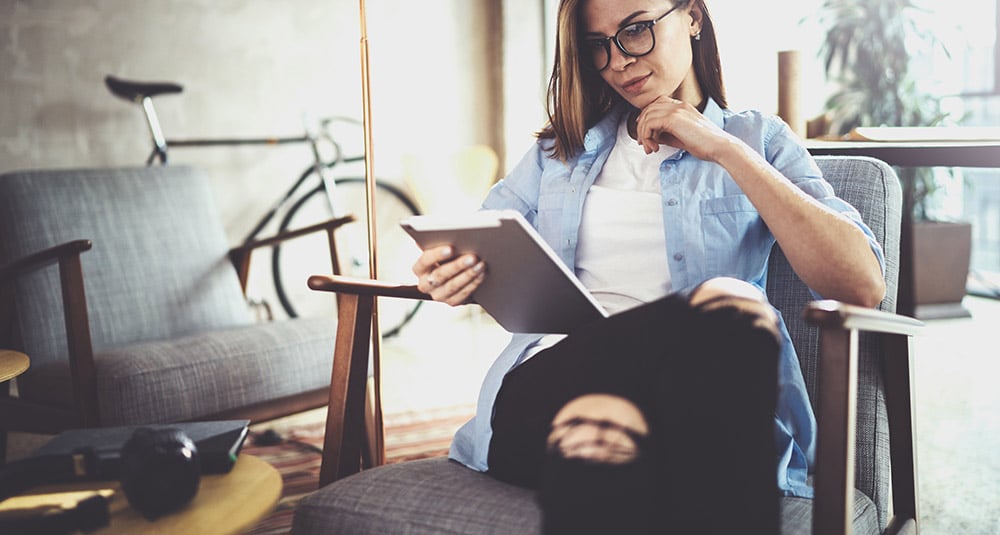Eine Frau sitzt in einem Sessel und schaut auf ein Tablet. Der Inhalt wurde automatisiert erstellt.