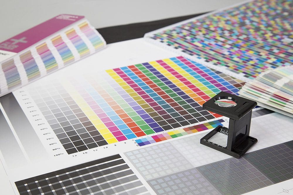 Mehrere gedruckte Bogen mit Farbfeldern auf denen eine Lupe steht