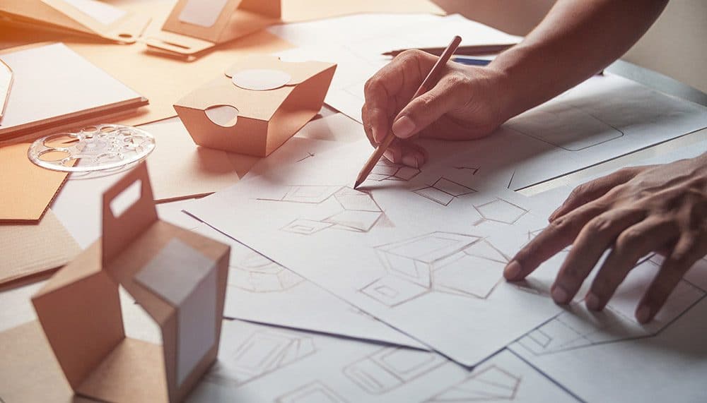 Man sieht eine Hand, die unterschiedliche Zeichnungen und Skizzen auf Papier malt