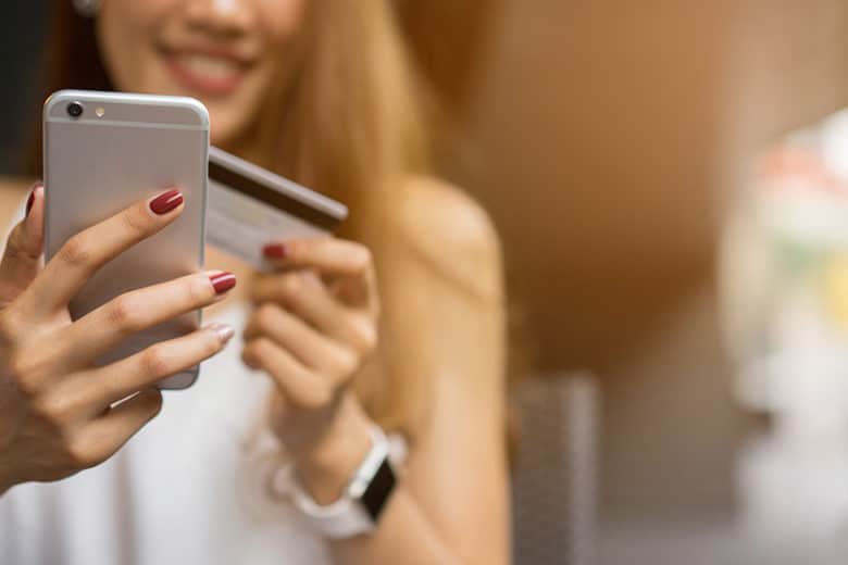 Eine Frau ist von vorne zu sehen, die ein silbernes Handy in der Hand hat und eine Kreditkarte in der anderen