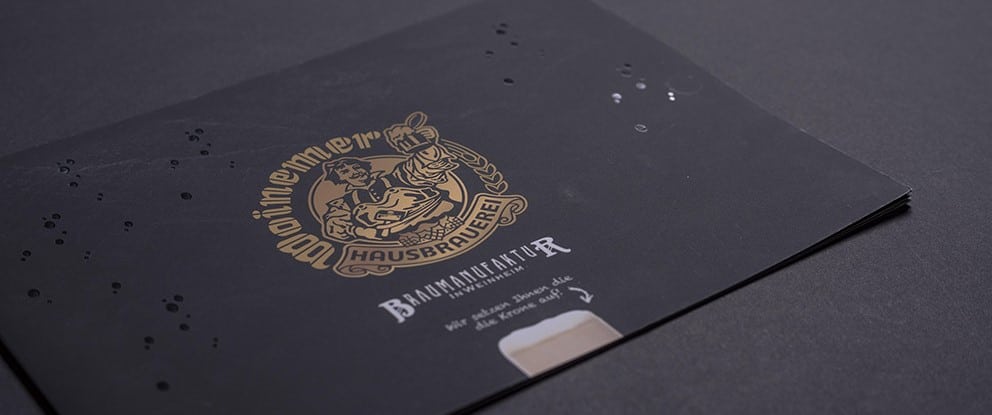 Druckereibroschüre veredelt mit Goldlack liegt auf grauem Untergrund