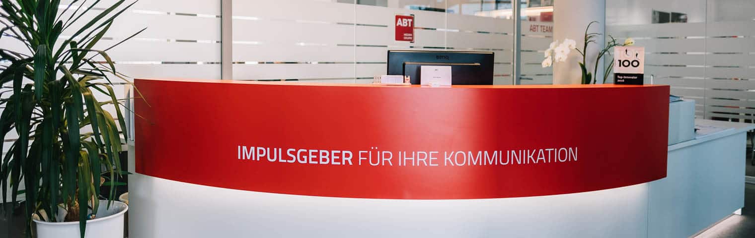 Empfangsbereich der ABT Mediengruppe. Beleuchteter Tresen mit der Aufschrift "Impulsgeber für Ihre Kommunikation" ist zu sehen