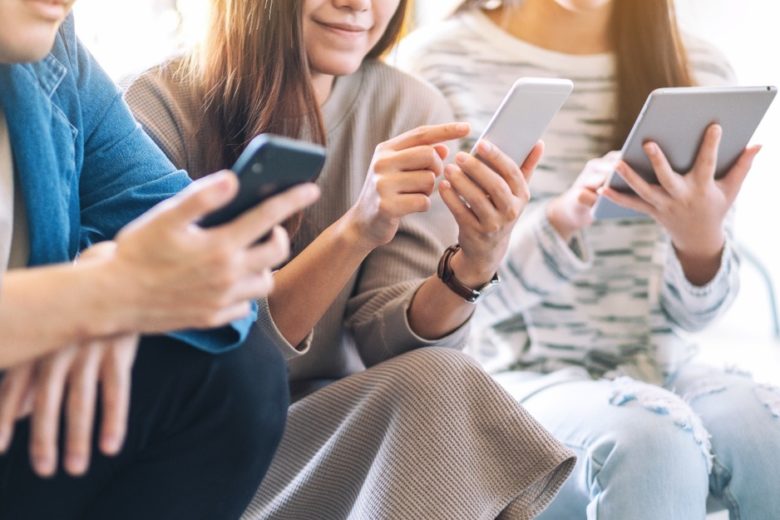 mehrere junge Menschen schauen lächelnd auf ihre Smartphones