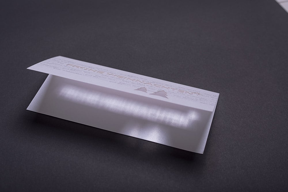 Eine aufgeklappt, querformatige Weihnachtskarte die hochwertig gedruckt und mit einer Laserstanzung im Titel veredelt ist