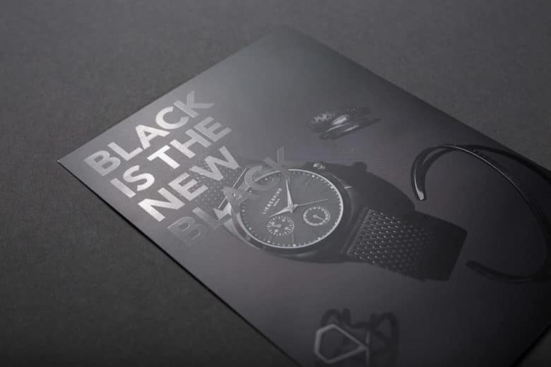 Ein DIN A4 Flyer, der vollflächig schwarz bedruckt ist und mit einer partiellen Lackierung den Satz "black is the new black" veredelt hat