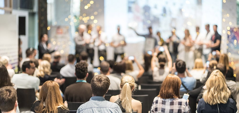 Es ist ein jubelndes Publikum vor einer Bühne bei einer Preisverleihung zu sehen.