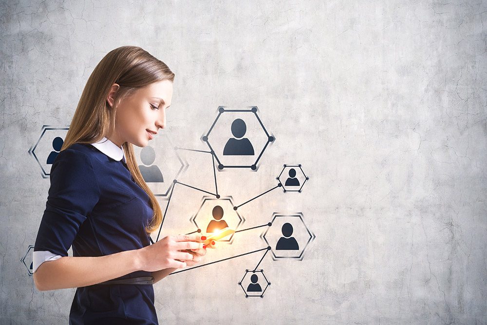 Eine junge Frau schaut auf ihr smartphone, darüber schweben mit sich verbunden Grafiken mit Personen drauf