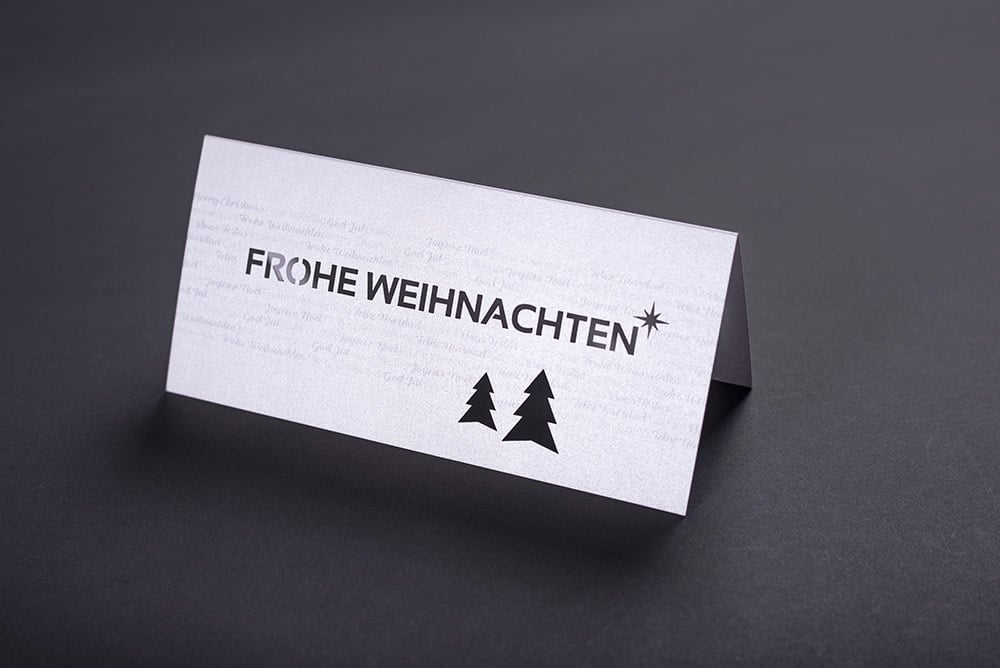 Eine aufgeklappt, querformatige Weihnachtskarte die hochwertig gedruckt und mit einer Laserstanzung im Titel veredelt ist
